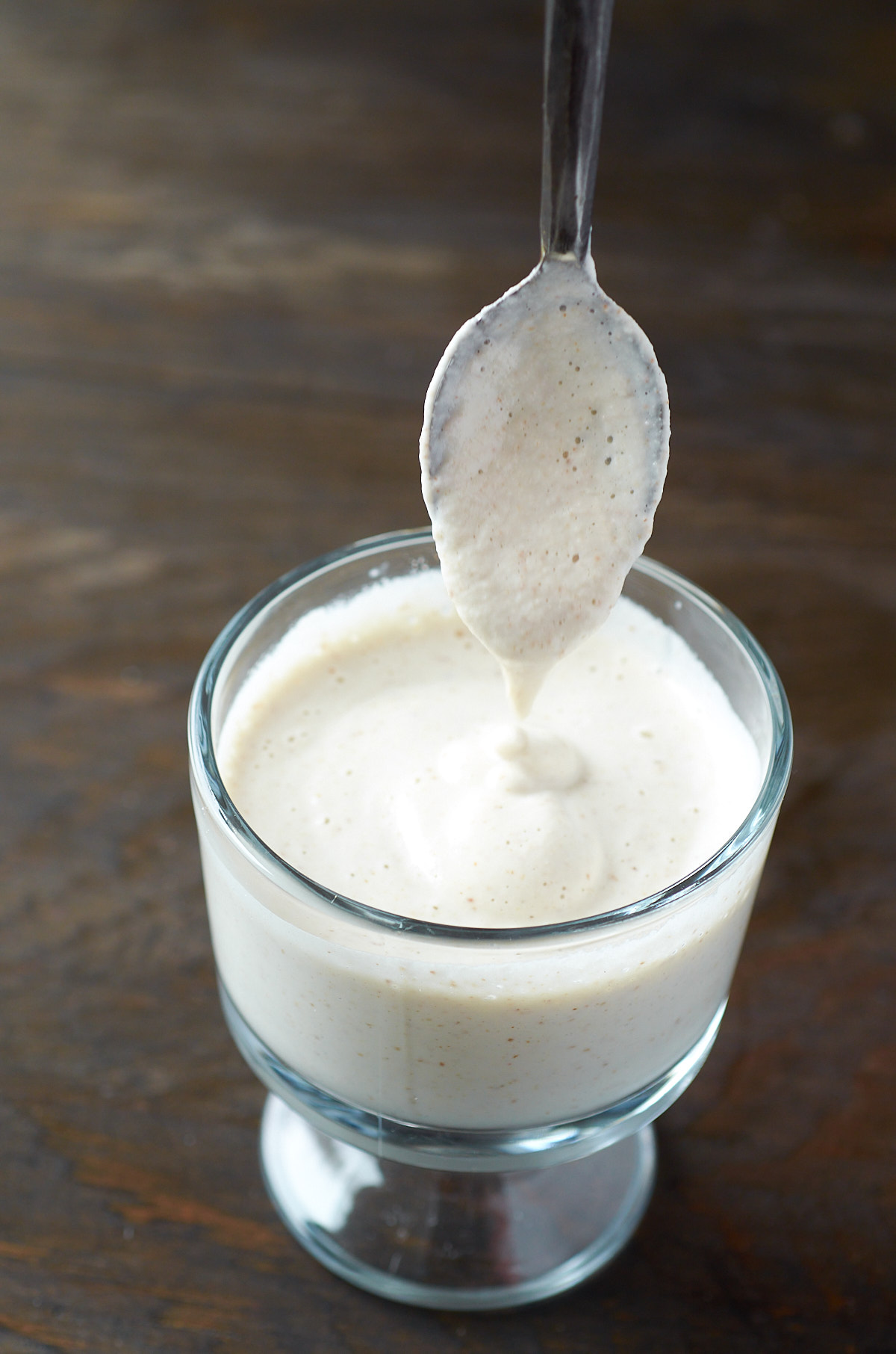 A metal spoon picking up a dollop of almond crema from a glass.