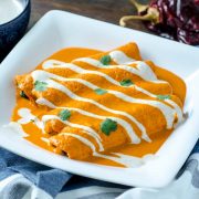 These spicy peanut sauce enchiladas, also known as encacahuatadas are smoky, creamy, savory, and full of umami. They are filled with sautéed mushrooms, and braised greens with hominy, bathed in a spicy guajillo-peanut sauce, and drizzled with almond crema.