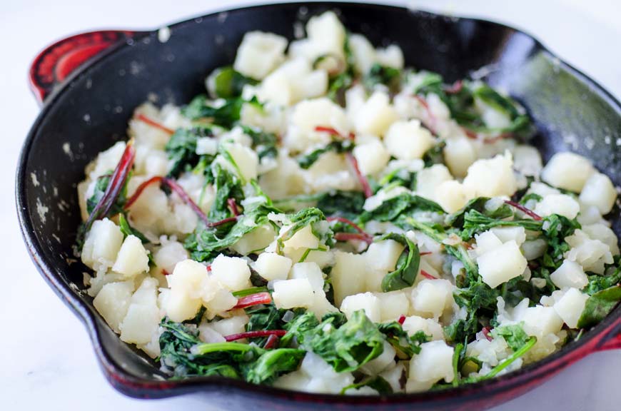 Braised greens and diced potatoes in a cast iron skillet.