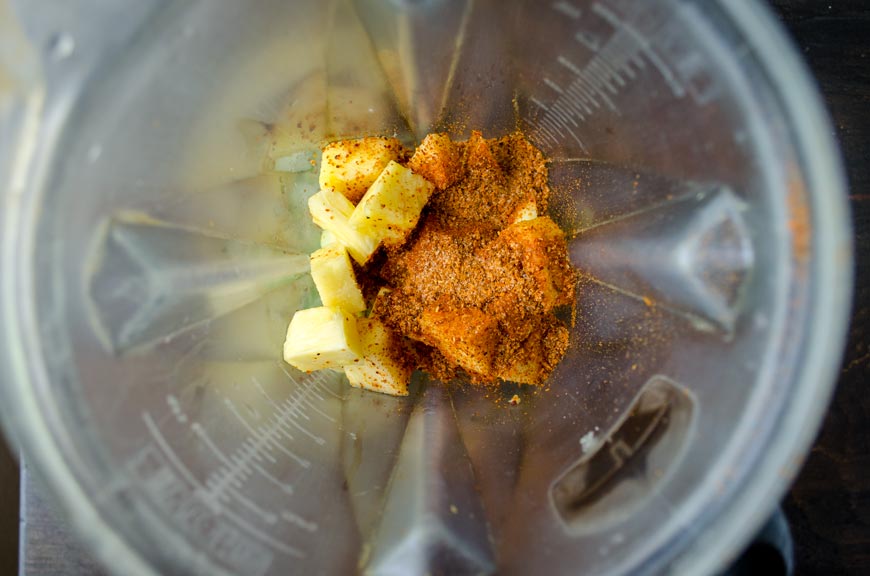Top view of a blender jar with pineapple chunks and spices.