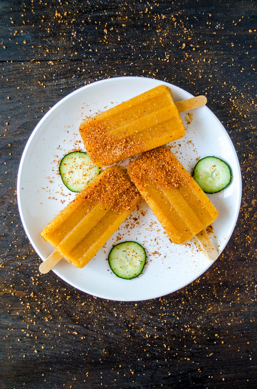Chipotle cucumber paletas on a white plate sprinkled with tajin.