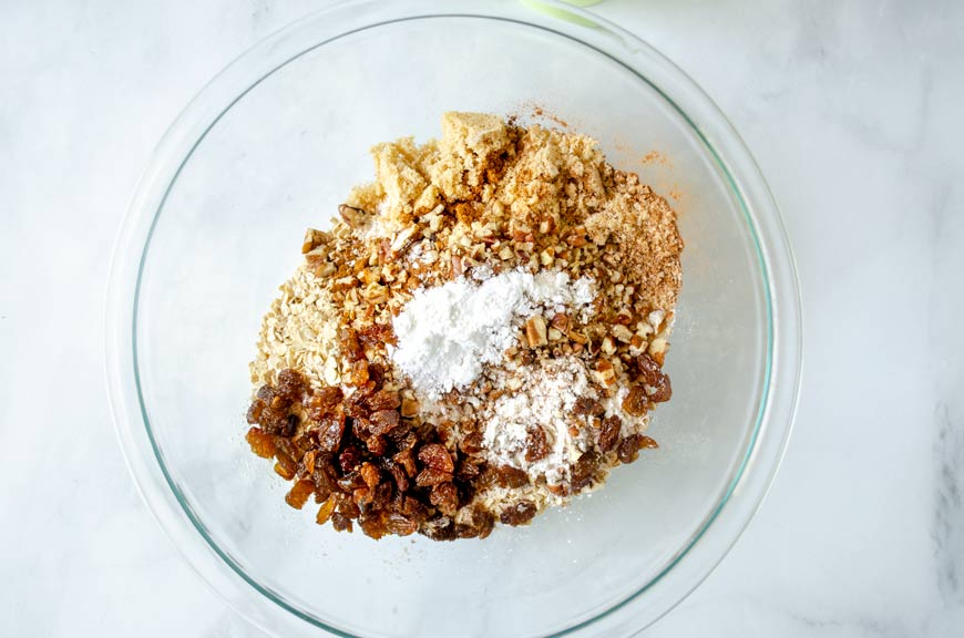 A glass mixing bowl with oats, sugar, and other additions.