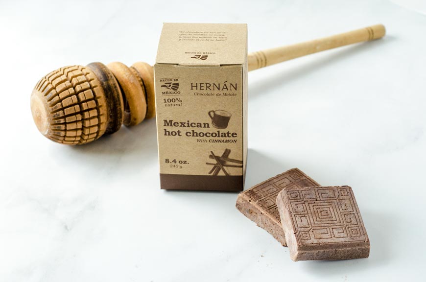 A box of Hernan Mexican chocolate with two unwrapped squares on a white surface.