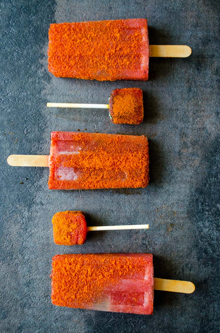 Tajin coated watermelon paletas on a blue background.