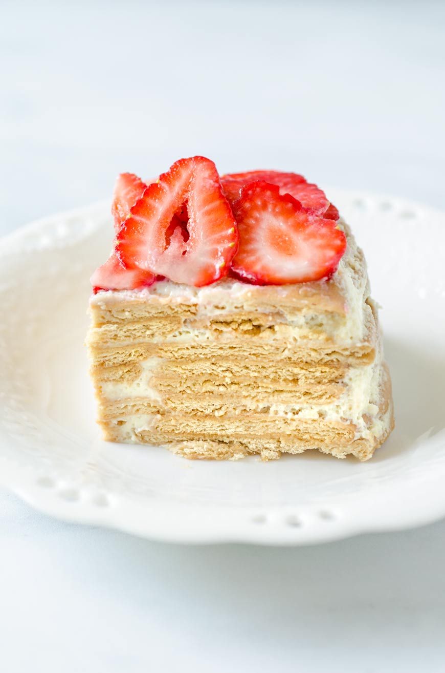 A square slice of key lime icebox cake topped with strawberries on a white dessert plate.