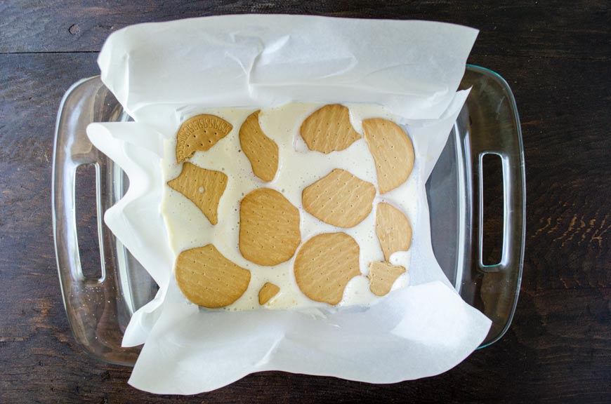 A square baking dish lined with parchment paper and a layer of cookies and cream.