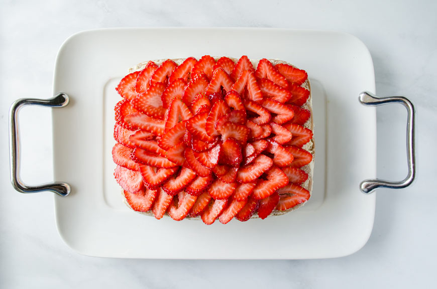 Top view of a square ice box cake topped with sliced strawberries on a square white platter.