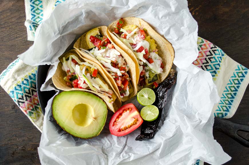 Vegan fish tacos in a cast iron pan with limes, tomato, and avocado