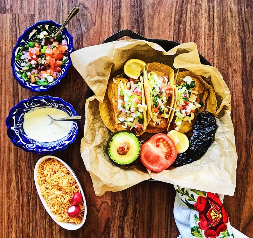 Vegan fish tacos in a cast iron pan with limes, tomato, and avocado