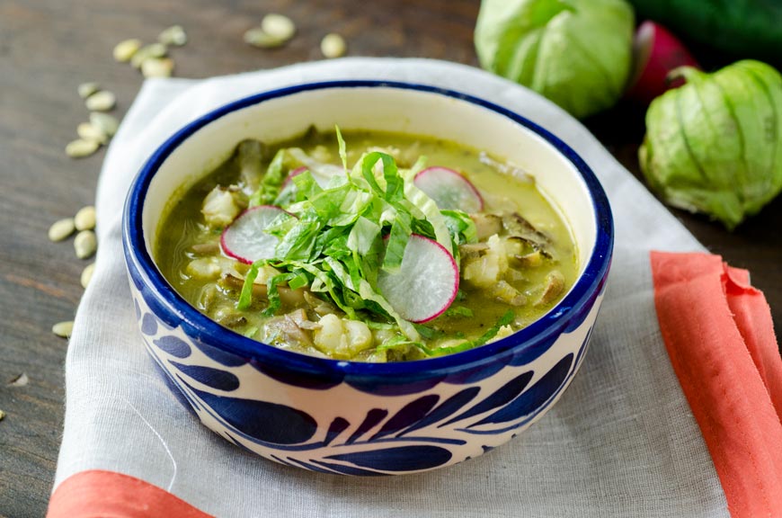 Vegan pozole verde topped with lettuce, radishes, and avocado in a blue and white talavera bowl