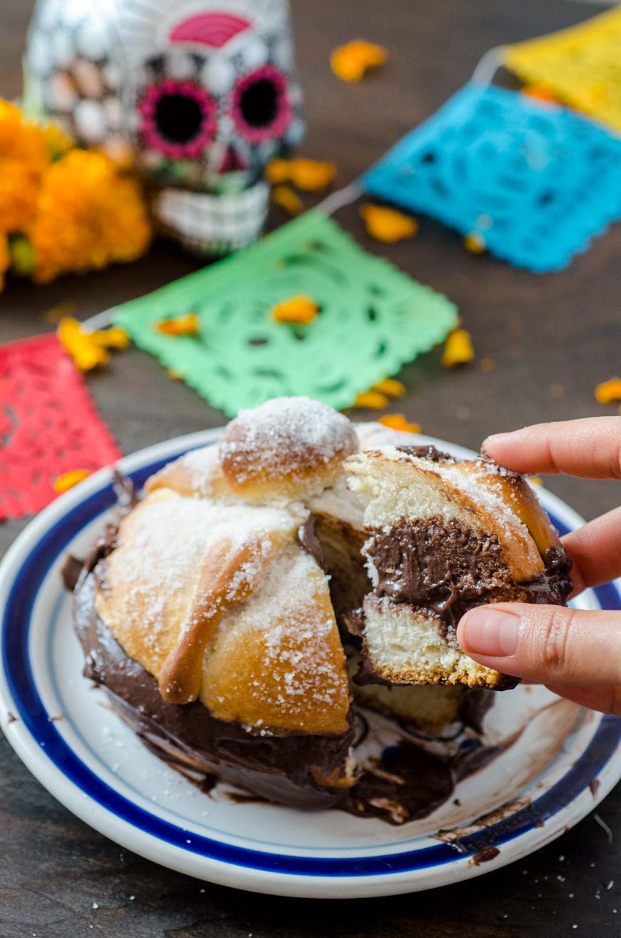 Vegan pan de muerto filled with chocolate, a hand is reaching in to take a piece