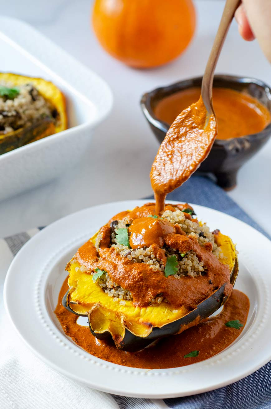 quinoa stuffed acorn squash and spoon pouring sauce on top of it