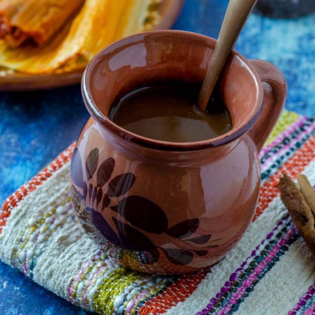 champurrado in a clay cup on a striped napkin