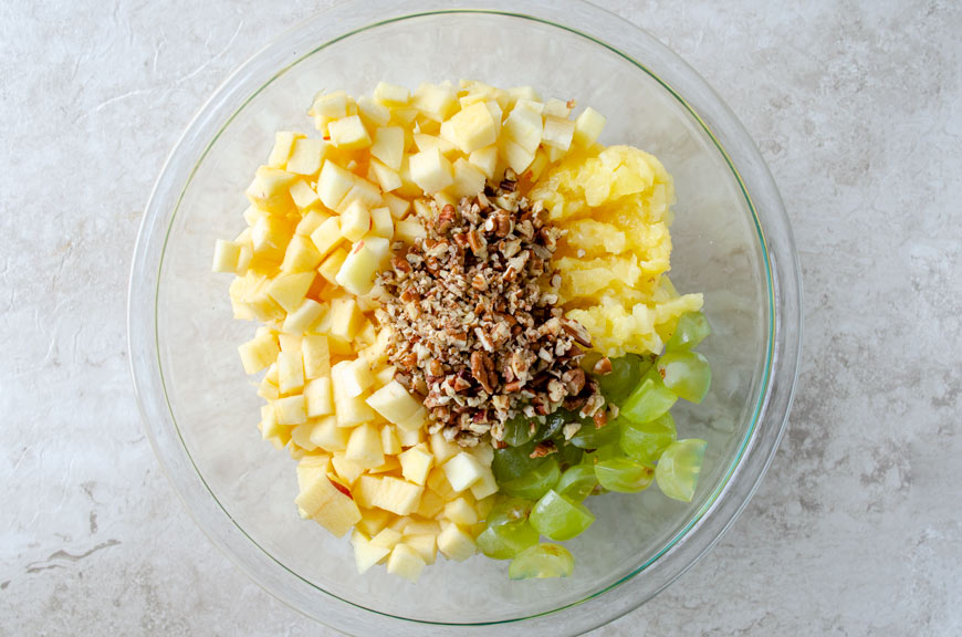 Glass bowl filled with apples, pineapple, grapes, and pecans.