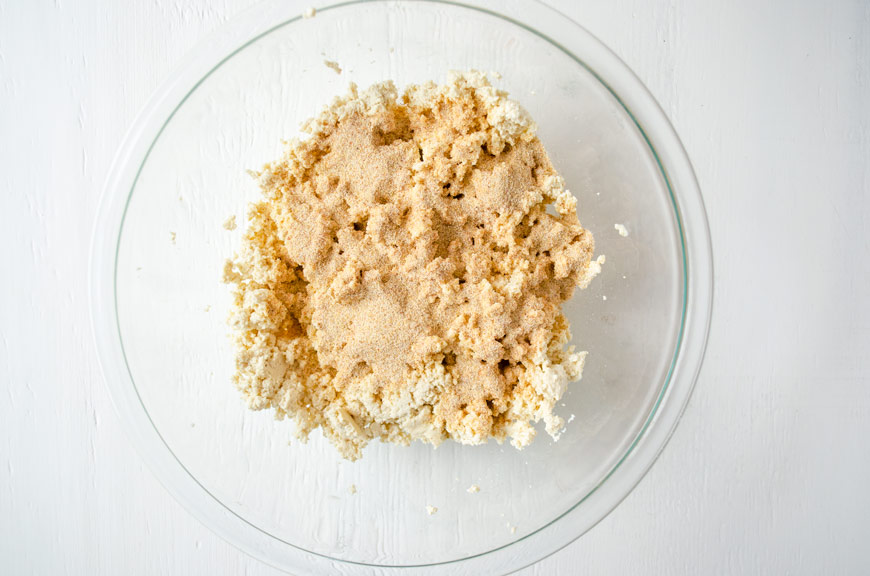 Spice mixture poured over crumbled tofu in a large glass bowl.