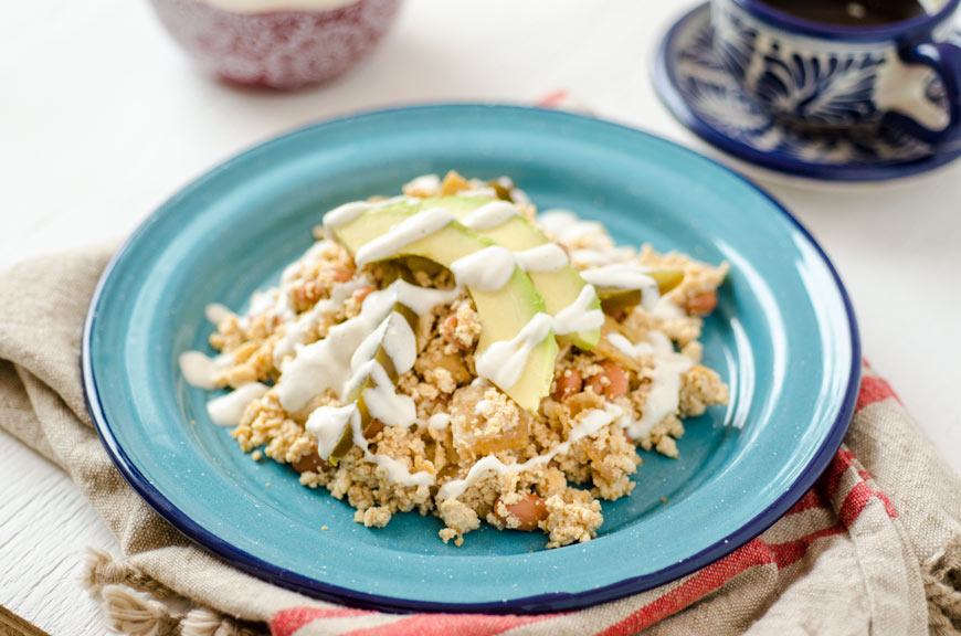 Tofu avocado scramble on a blue plate with a cup of coffee beside it