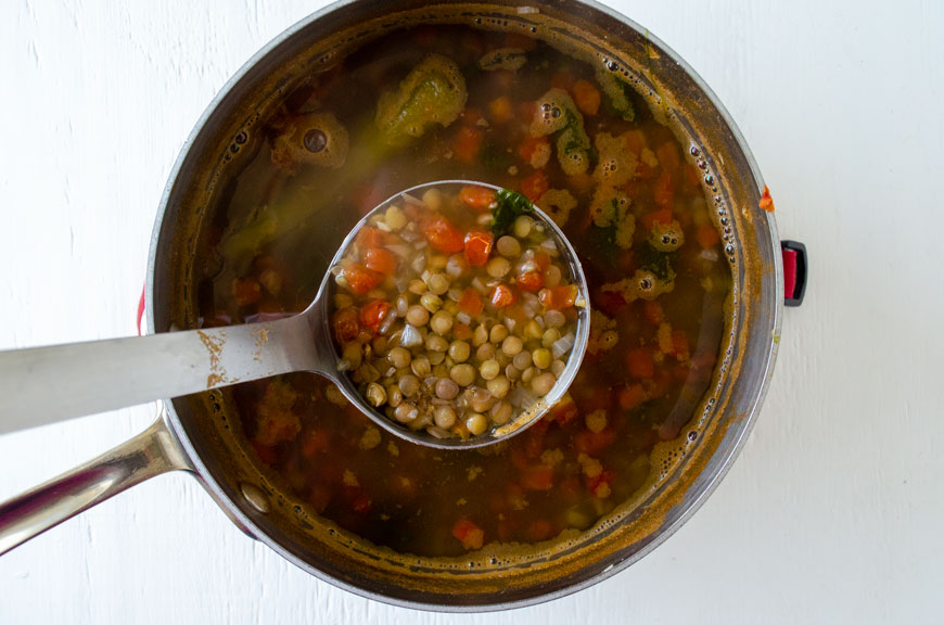 A ladle full of vegan lentil soup suspended on top of sauce pot full of lentils.