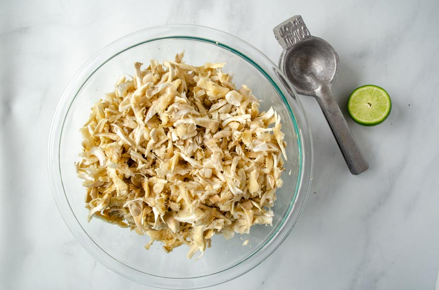 Shredded oyster mushrooms in a glass bowl. A lime squeezer and lime beside it. 