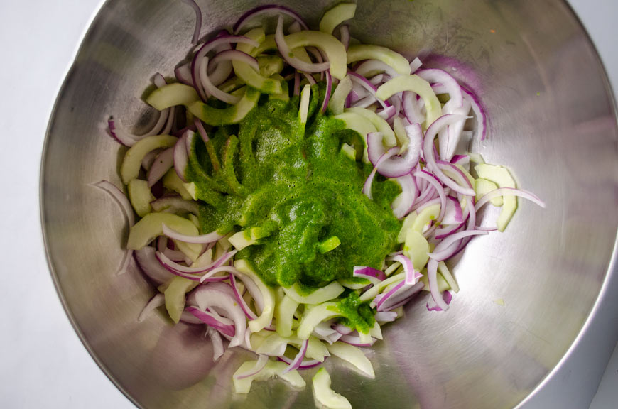 Serrano-lime salsa poured over cucumber and onion in large stainless steel bowl.