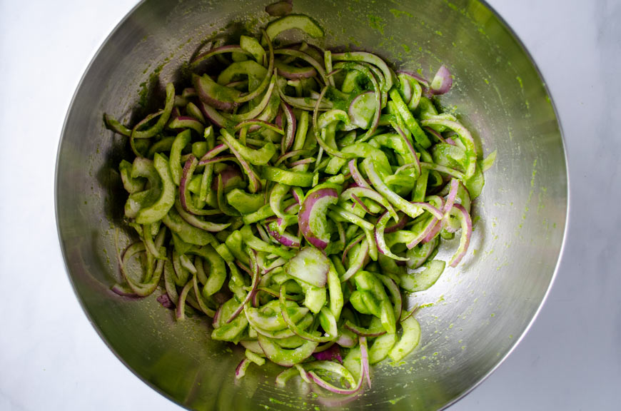 Salsa mixed with red onion and cucumbers in a large stainless bowl. 