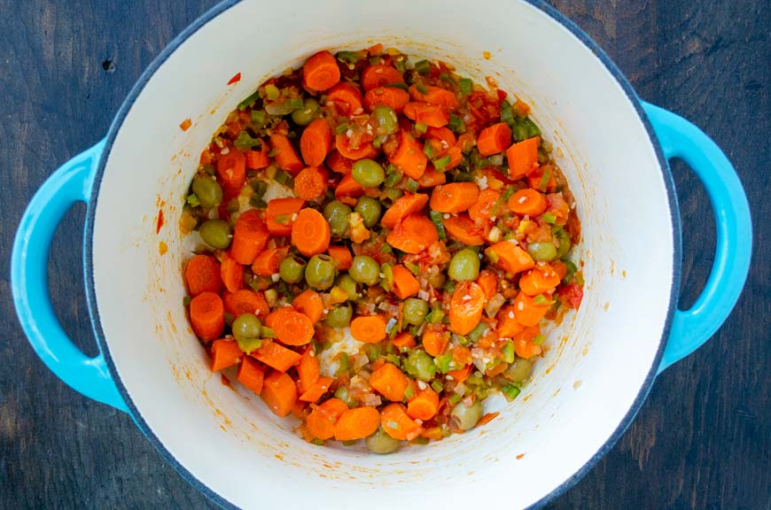 White pot with onion, carrots, tomatoes, and anaheim chile.