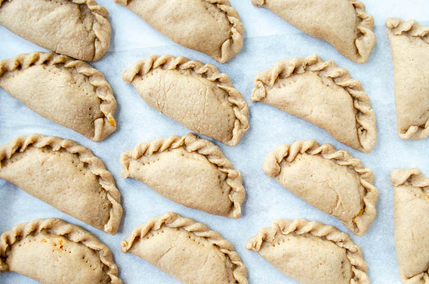 Empanadas ready to bake on a sheet tray.