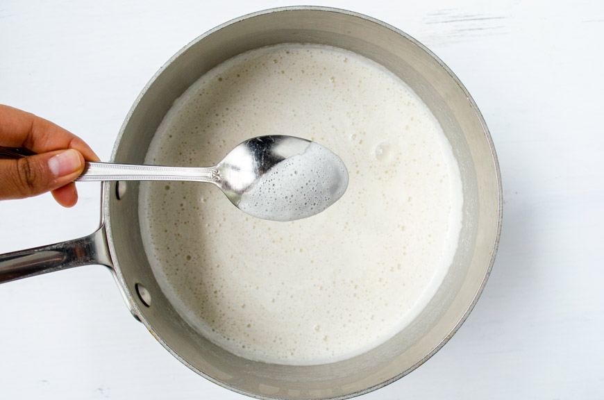 a spoon dipped into the thickened milk mixture showing it coating the back of the spoon