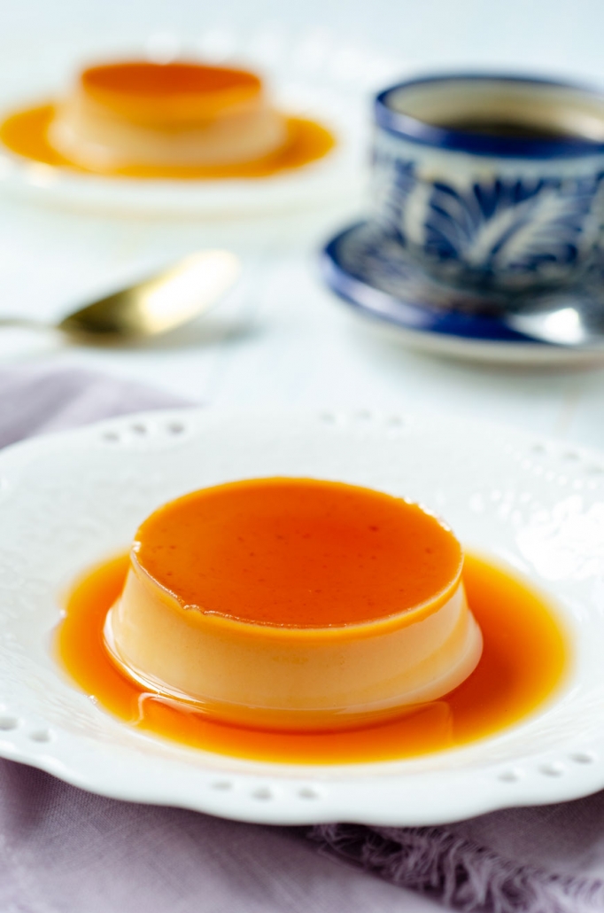 vegan flan on a small white laced plate with a coffee and another flan in the background