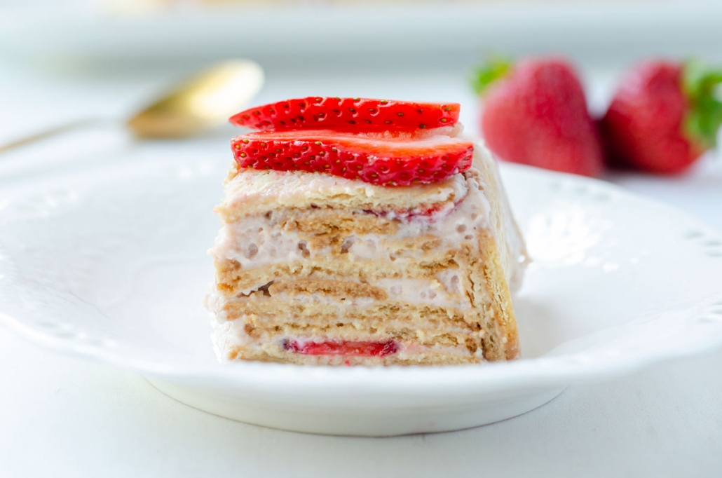 Close up of a slice of vegan carlota de fresa topped with sliced strawberries on a white plate.