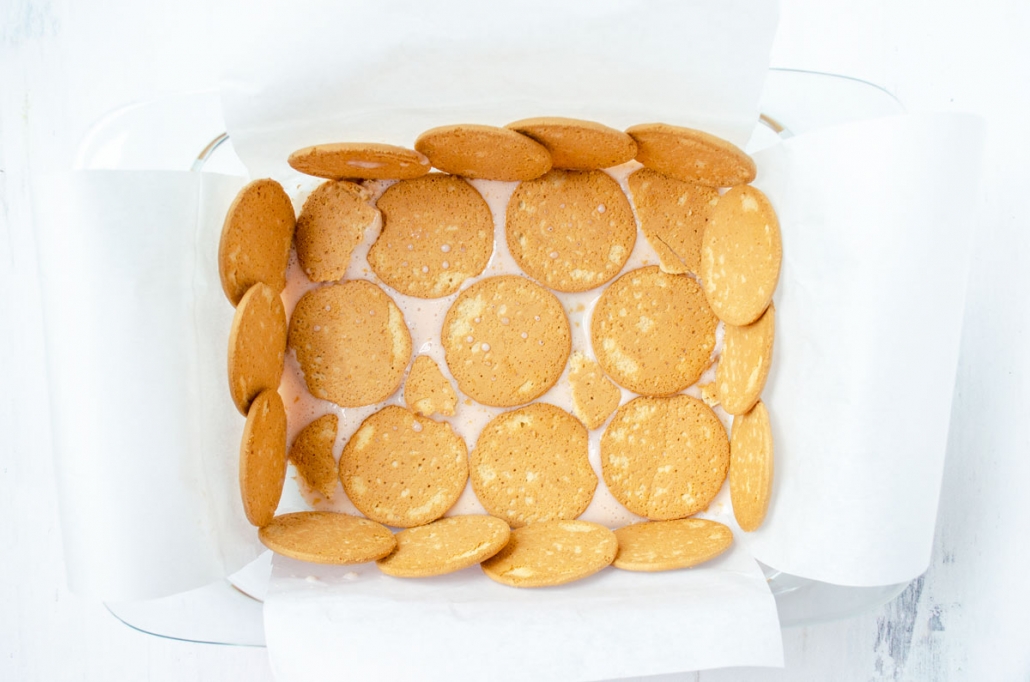 Parchment paper lined glass baking dish lined with rows of Maria cookies.