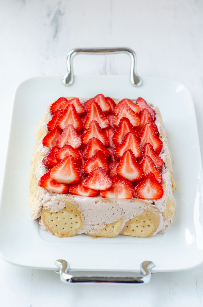 Vegan carlota de fresa, strawberry iced box cake topped with sliced strawberries, on a white serving tray.