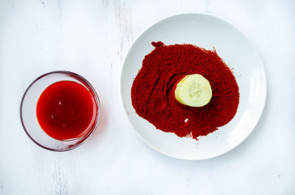 a glass bowl with chamoy and a white plate with chile powder and cucumber cup being dipped in