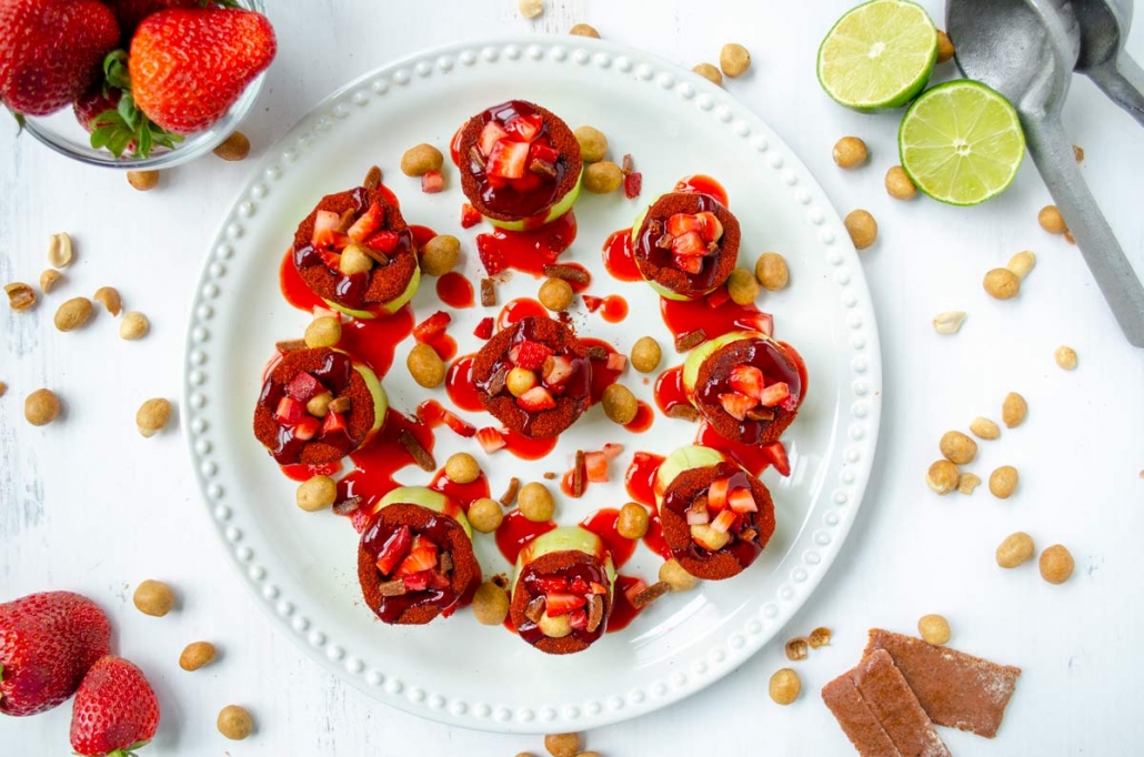 pepinos locos on a white plate with chamoy poured over them surrounded by strawberries and limes