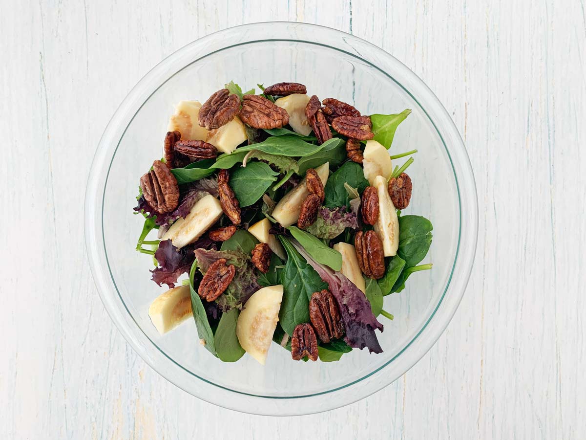 glass bowl with mixed greens, guava, and candied pecans