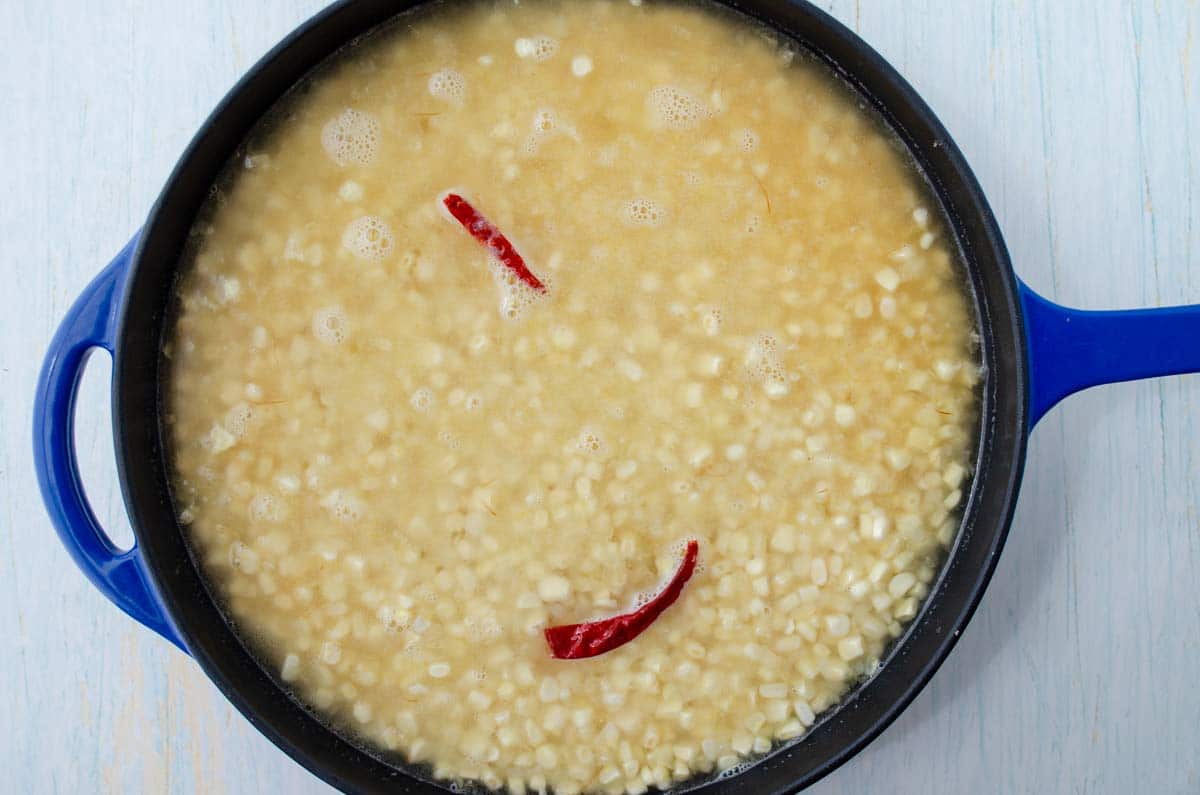 Blue saute pan with veggie broth added to corn kernels