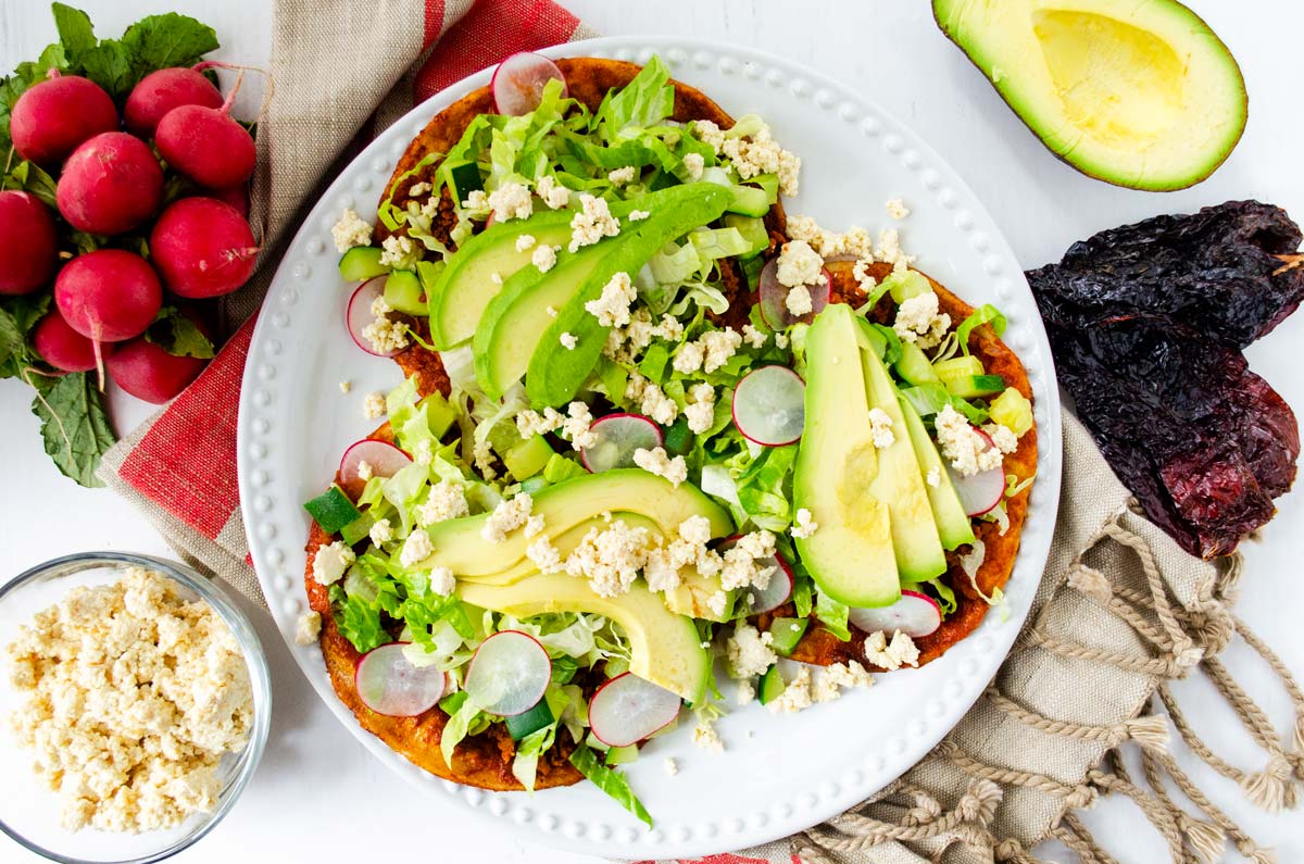 enchiladas de suelo on a white plate surrounded by radishes, dried chiles, and avocado