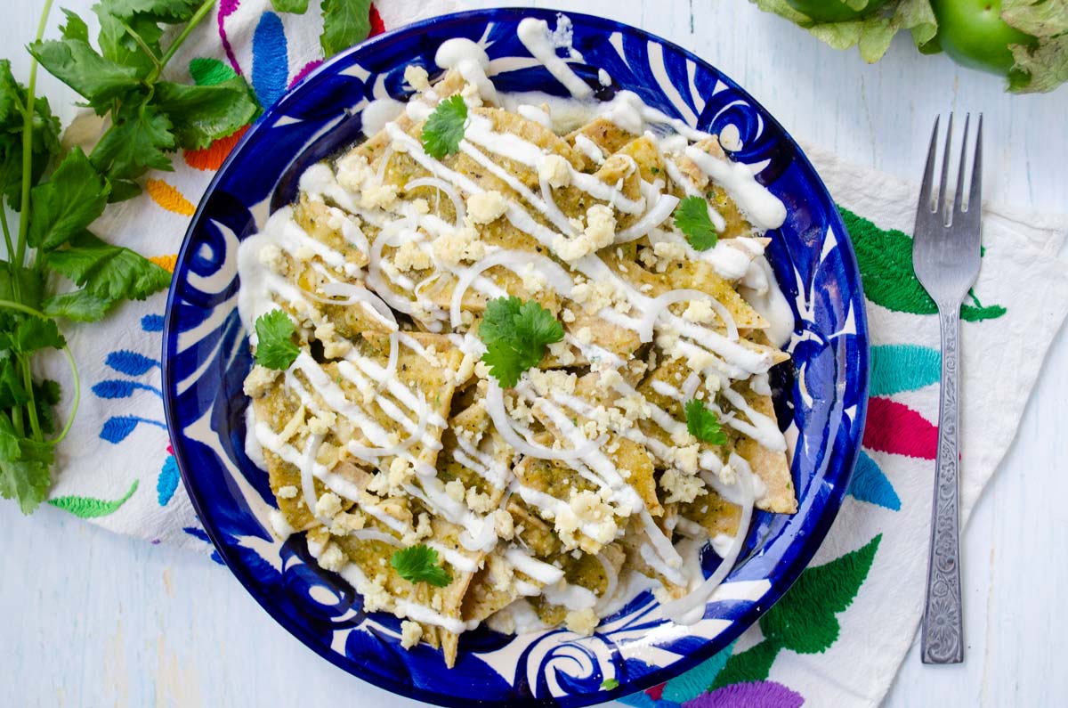 a bright blue plate with chilaquiles verdes topped with crema and cheese