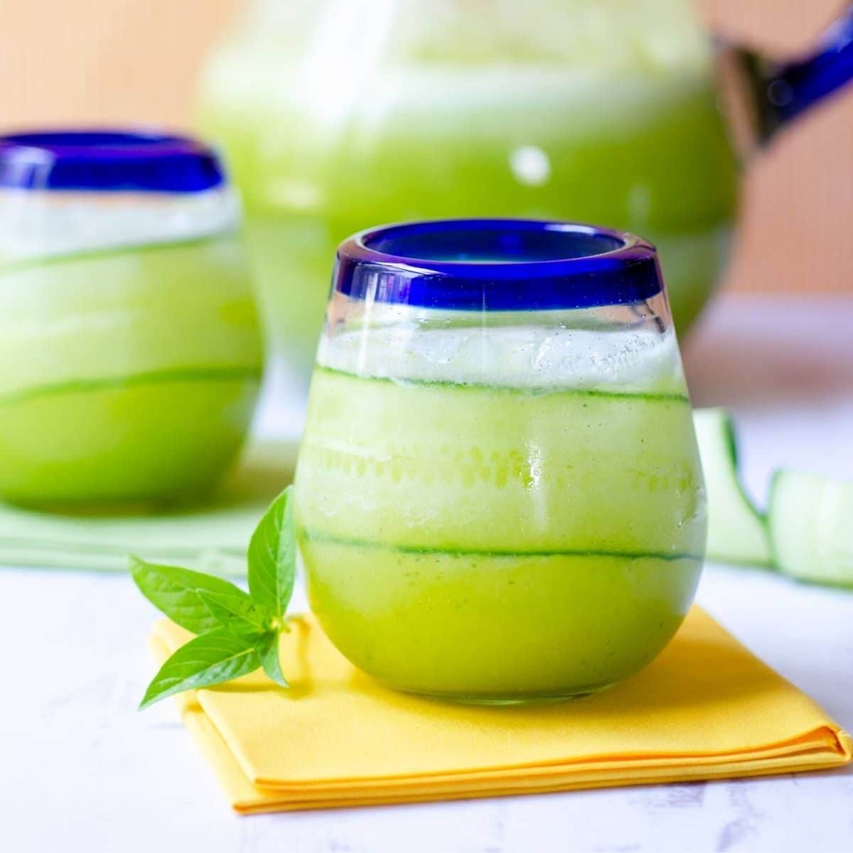 two glasses filled with pinaepple cucumber agua fresca with a pitcher behind