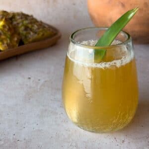 glass of pineapple fermented drink with a pineapple leaf as a garnish