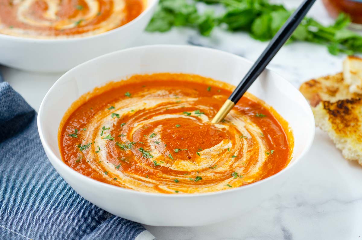 bowl of tomato soup with cream on top and a black and gold spoon