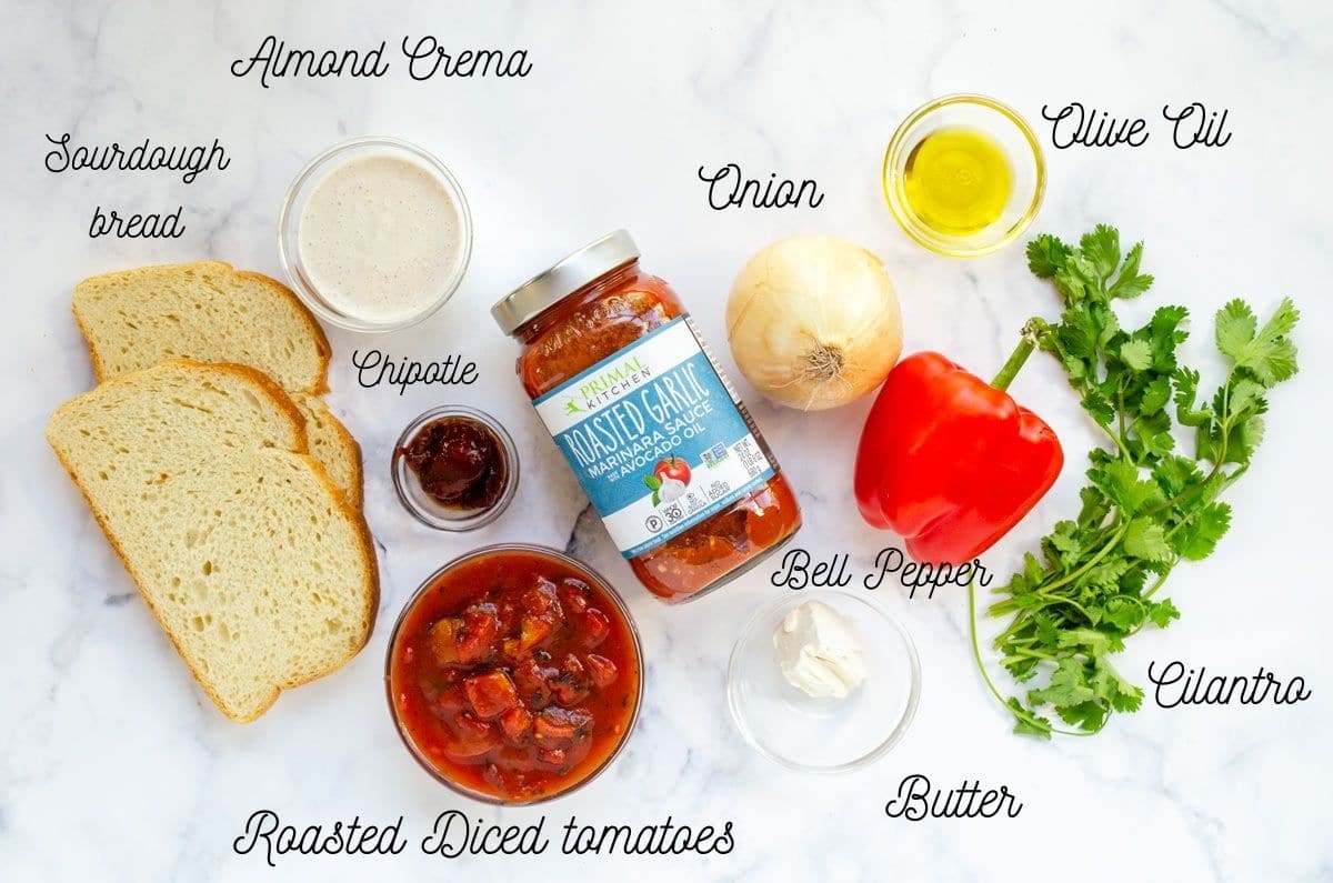 ingredients for tomato soup olive oil, cilantro, bell pepper, onion, butter, diced tomatoes, chipotle, almond crema, sourdough bread