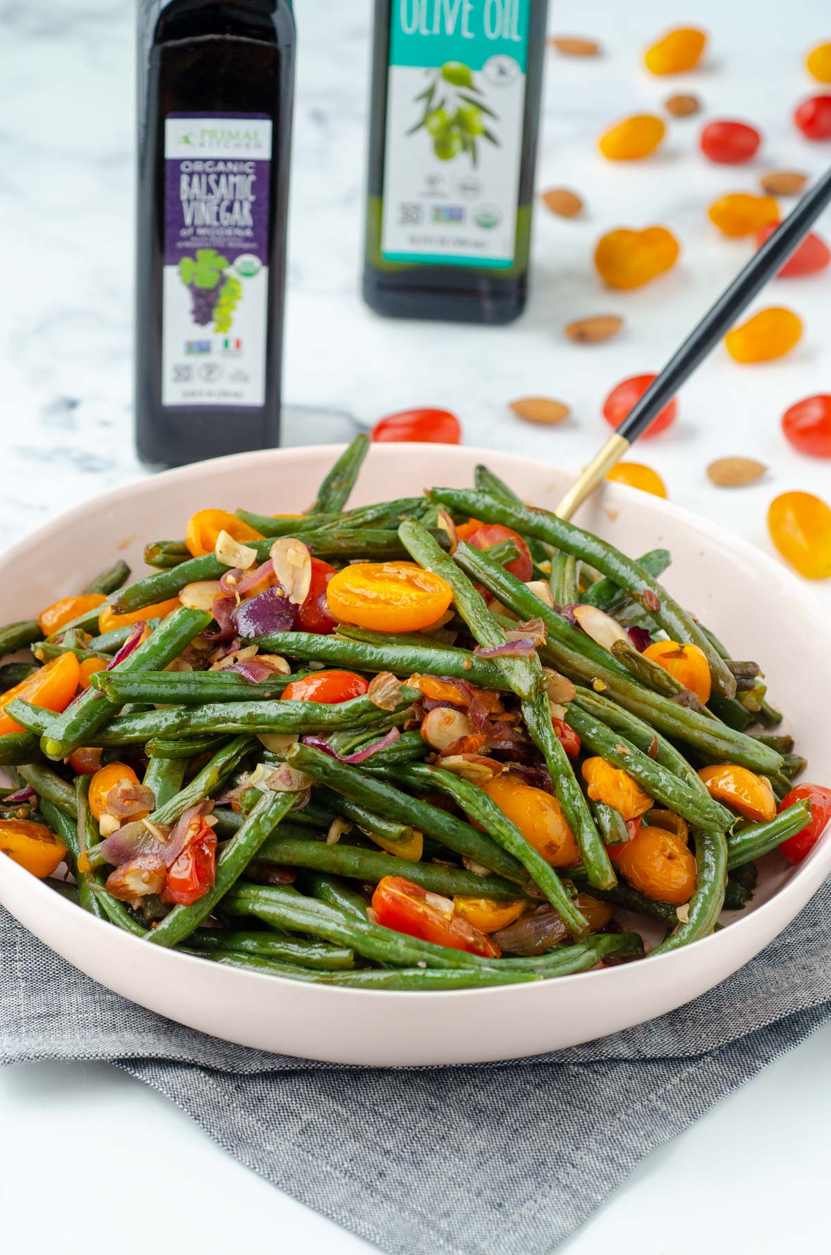 bowl of green beans on a gray napkin with a bottle of balsamic behind it