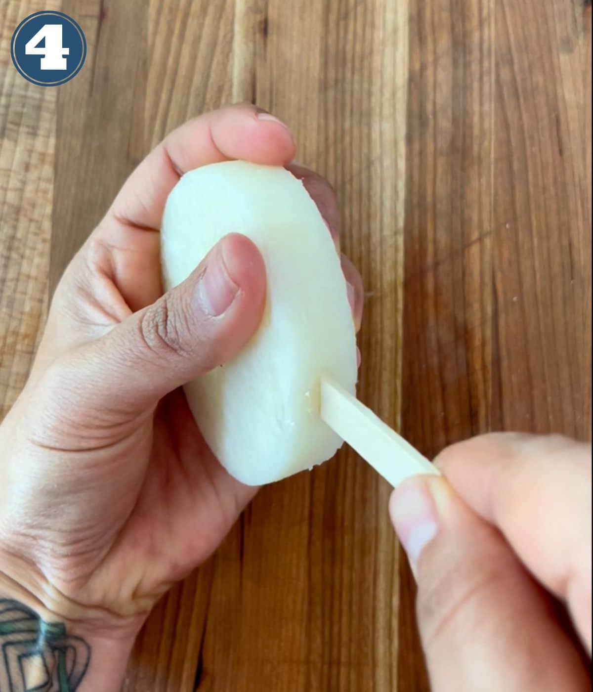 A popsicle stick being inserted into a slice of jicama.