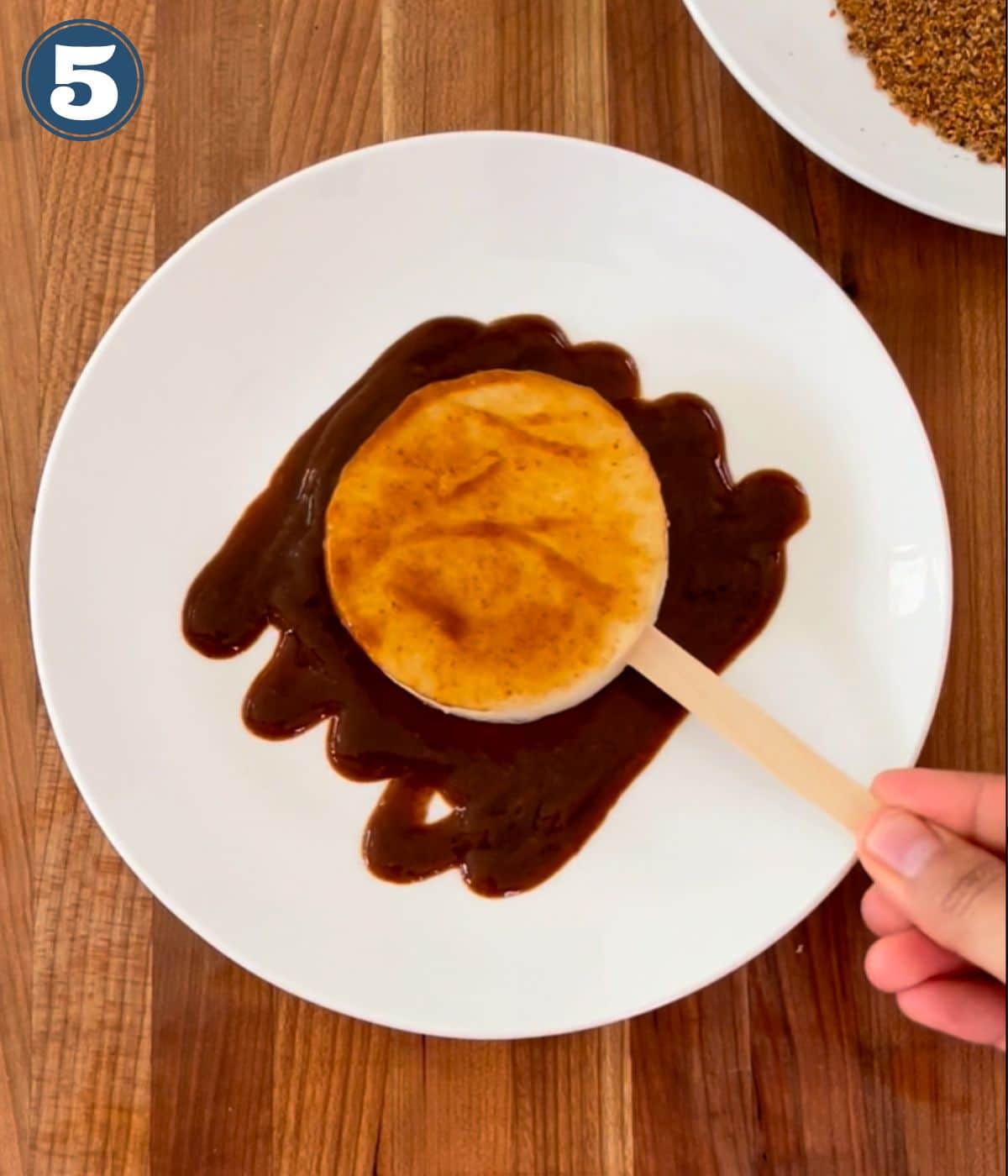 Slice of jicama on a popsicle stick being dipped in chamoy.