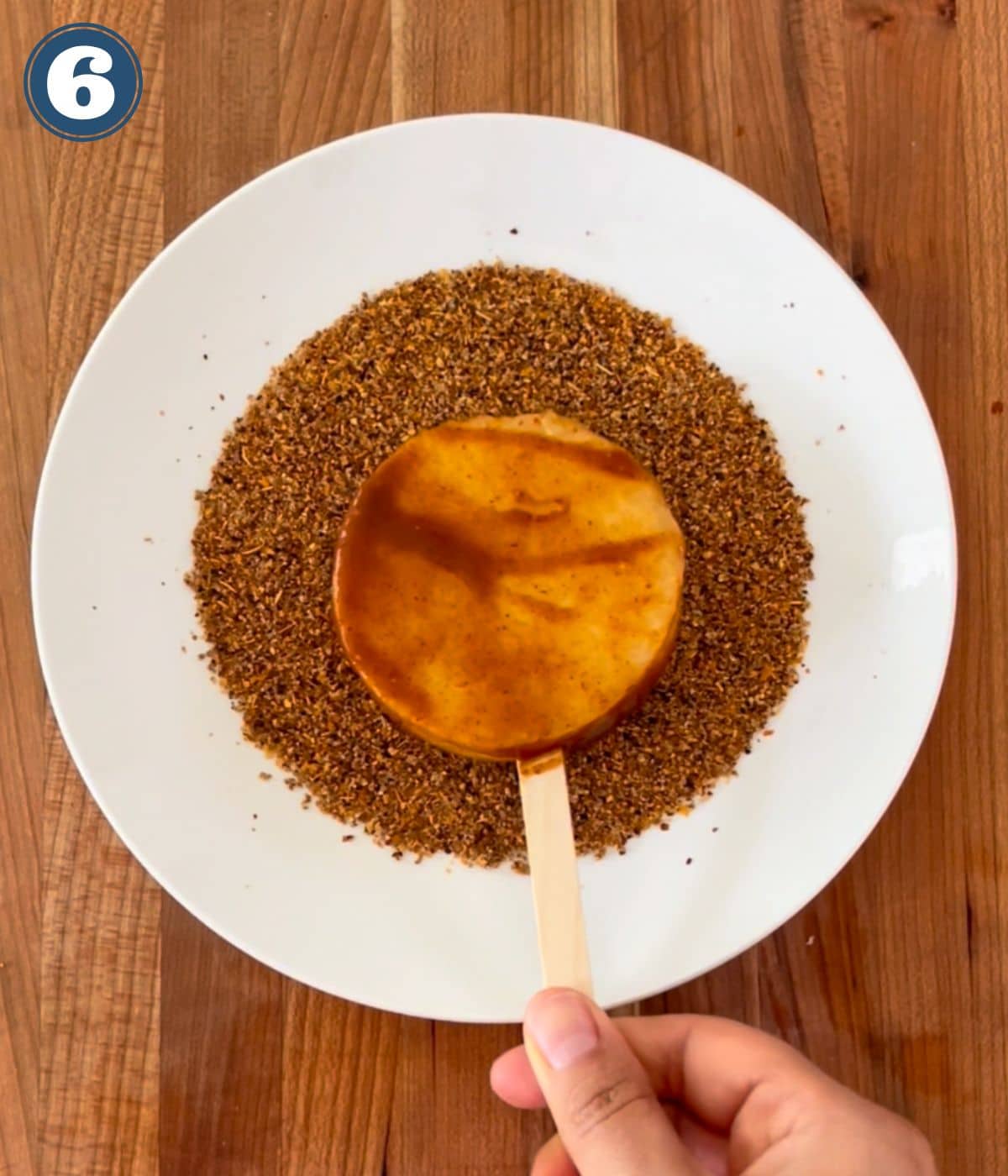 A slice of jicama covered in chamoy being dipped in chile powder.