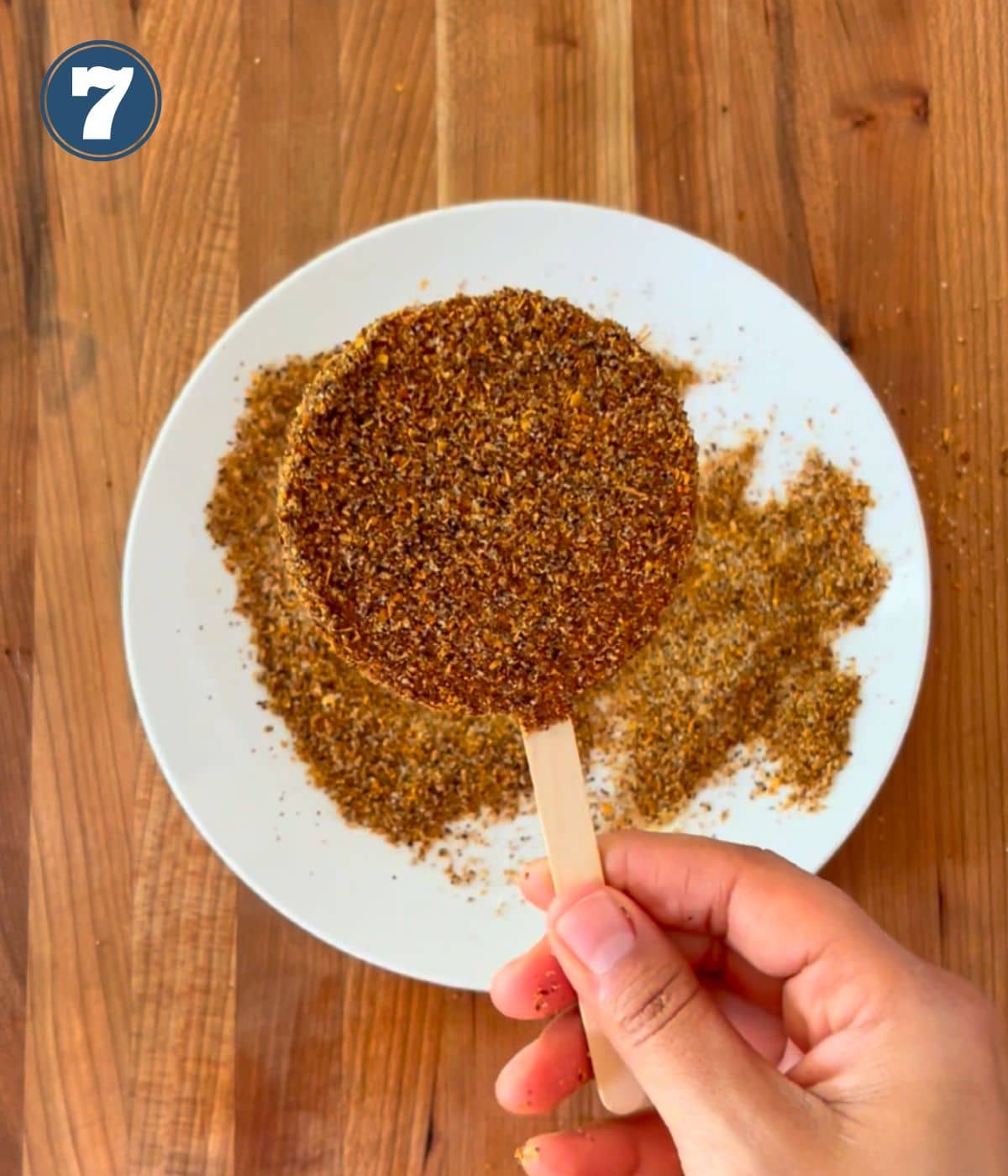 A hand holding a jicaleta over a plate with chile powder.