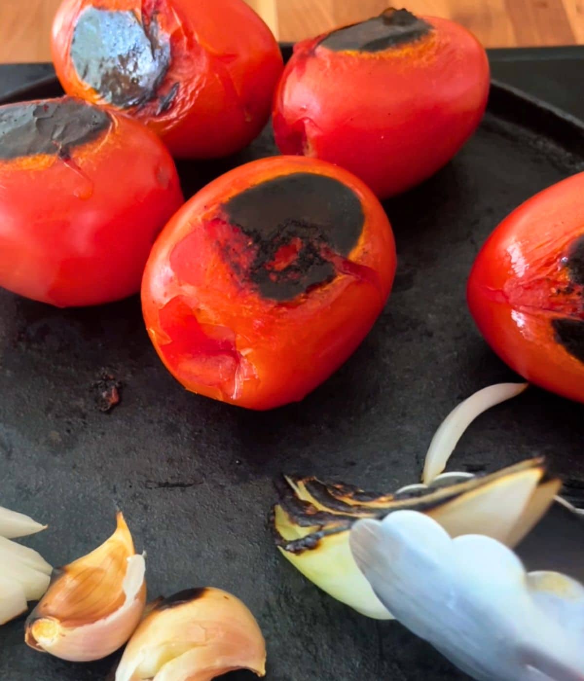 tomatoes, onion, and garlic roasting on a cast iron comal