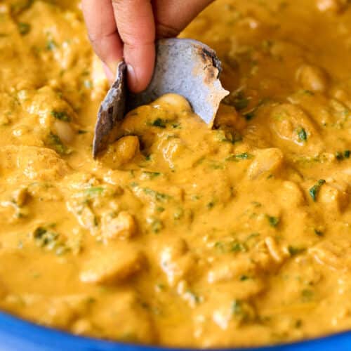 a blue corn tortilla dipping into a skillet with beans