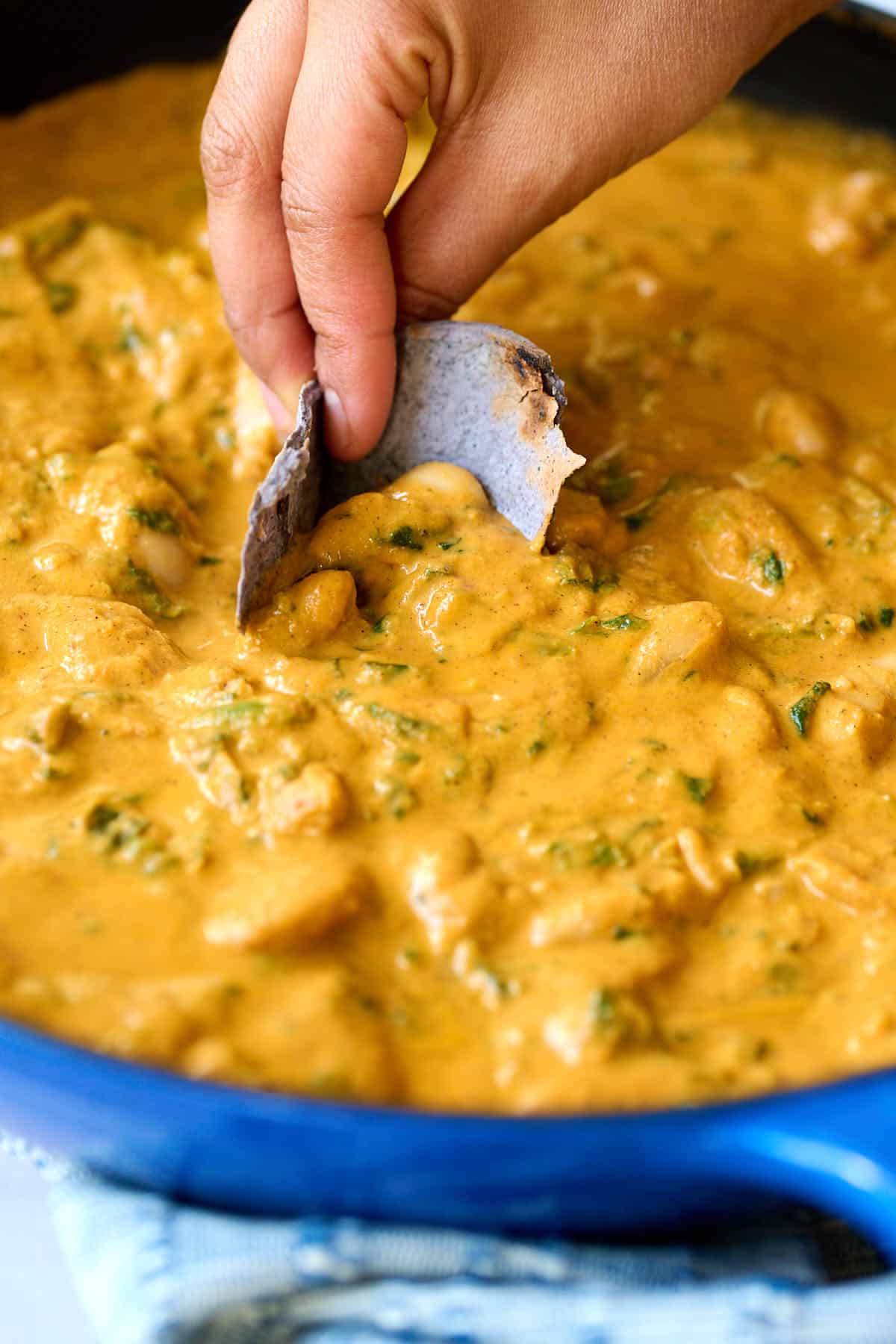 a blue corn tortilla dipping into a skillet with beans