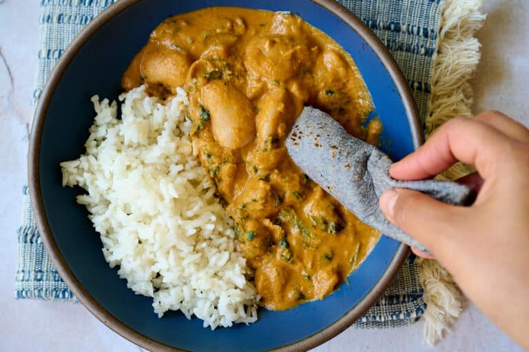 a blue corn tortilla dipping into creamy chipotle beans in a blue plate.